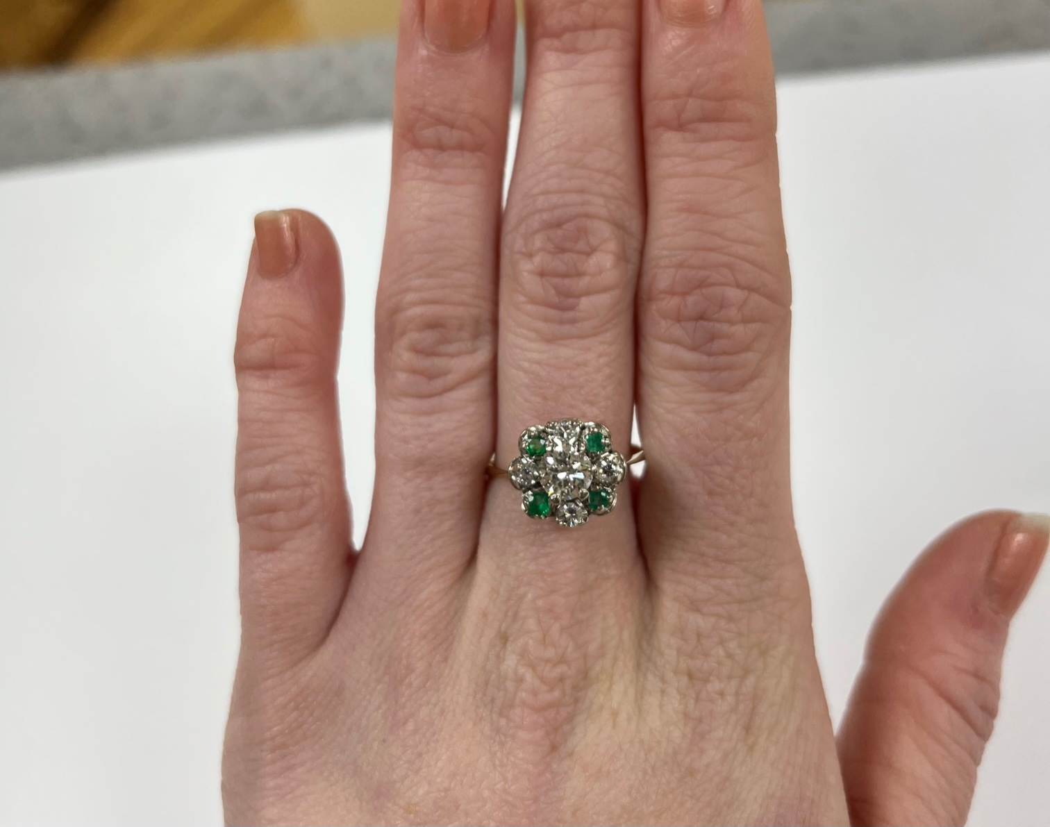 A yellow metal, diamond and emerald set flower head cluster ring, size P, gross weight 4 grams, the central diamond measuring approximately 5.5mm in diameter.